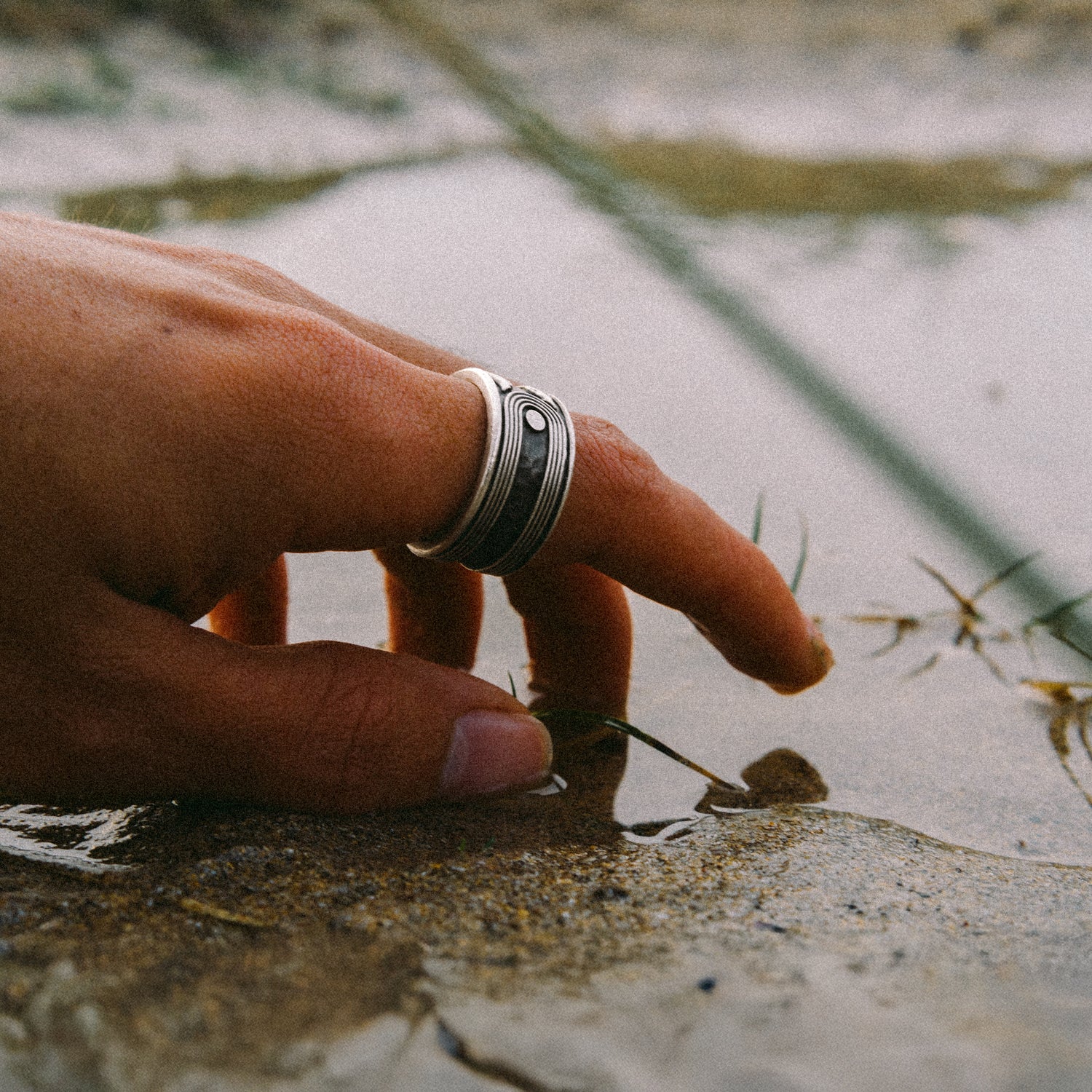 Hand wearing a ring touching water and sand