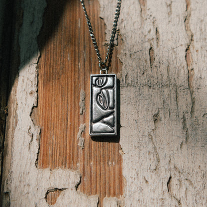 Solaque Silent Gaze handmade sterling silver face design pendant jewellery on a rustic wooden surface
