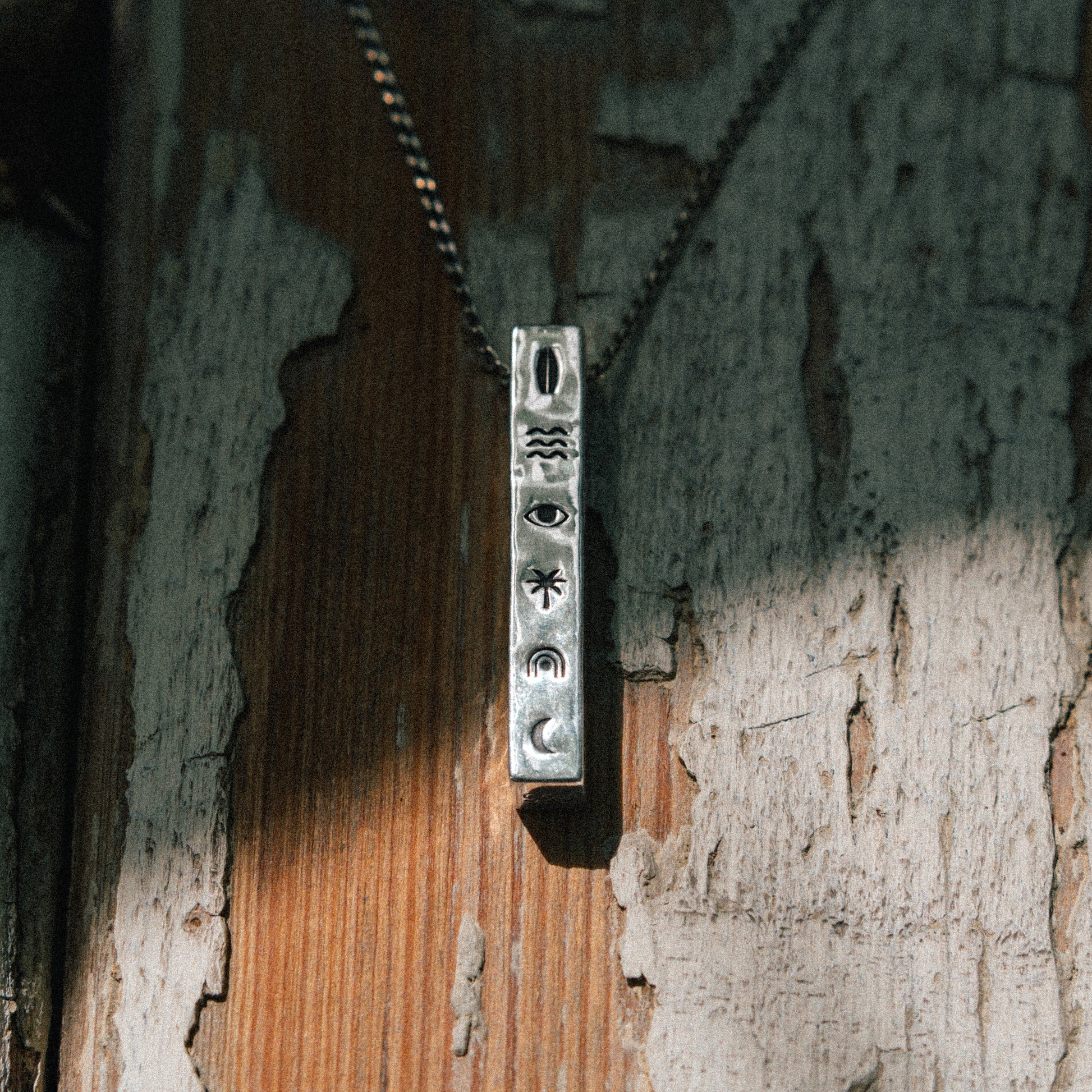 Solaque Wanderer's Script handmade sterling silver icon design pendant jewellery on a rustic wooden surface
